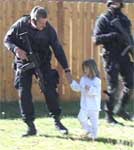 Photo of a child being removed from a home by a SWAT officer.